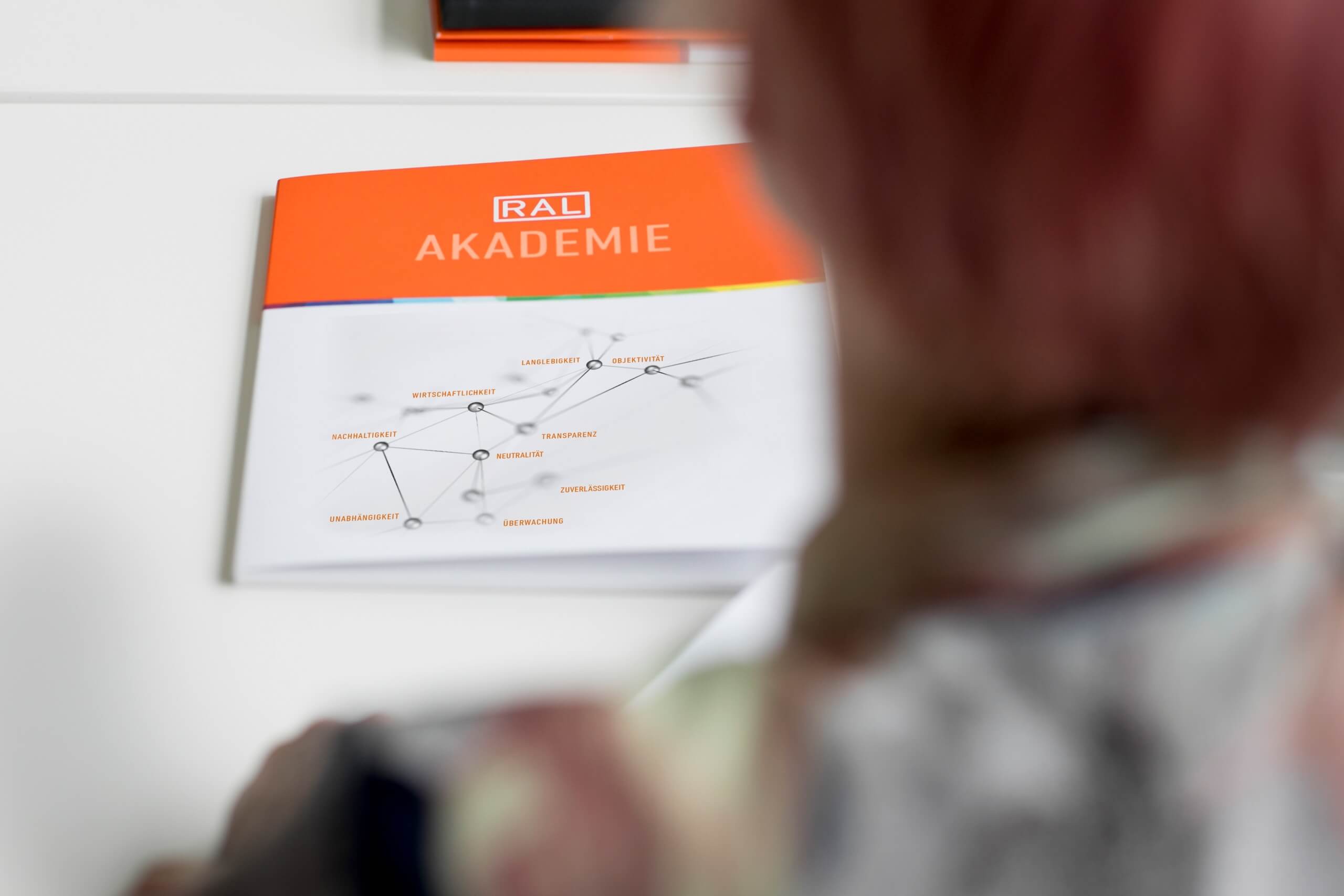 Blick über die Schulter auf eine RAL Akademie Broschüre