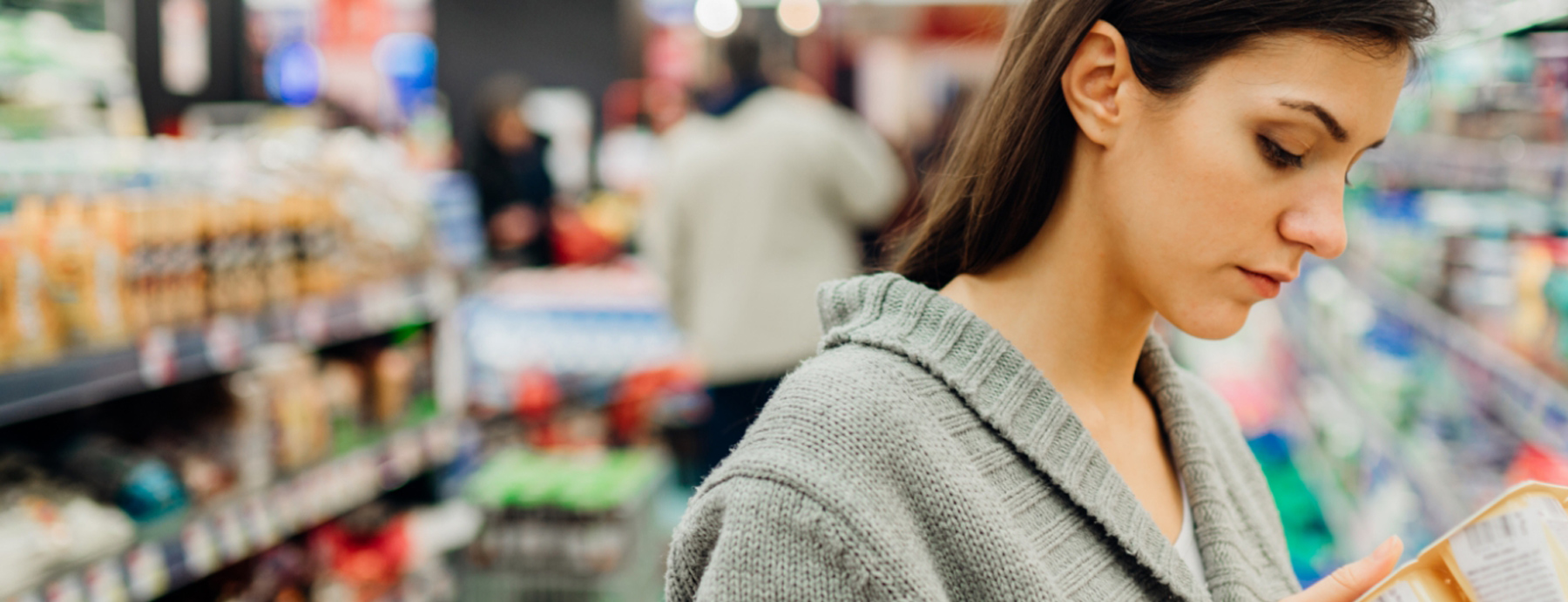 Frau vor Lebensmittelregalen liest auf einer Verpackung