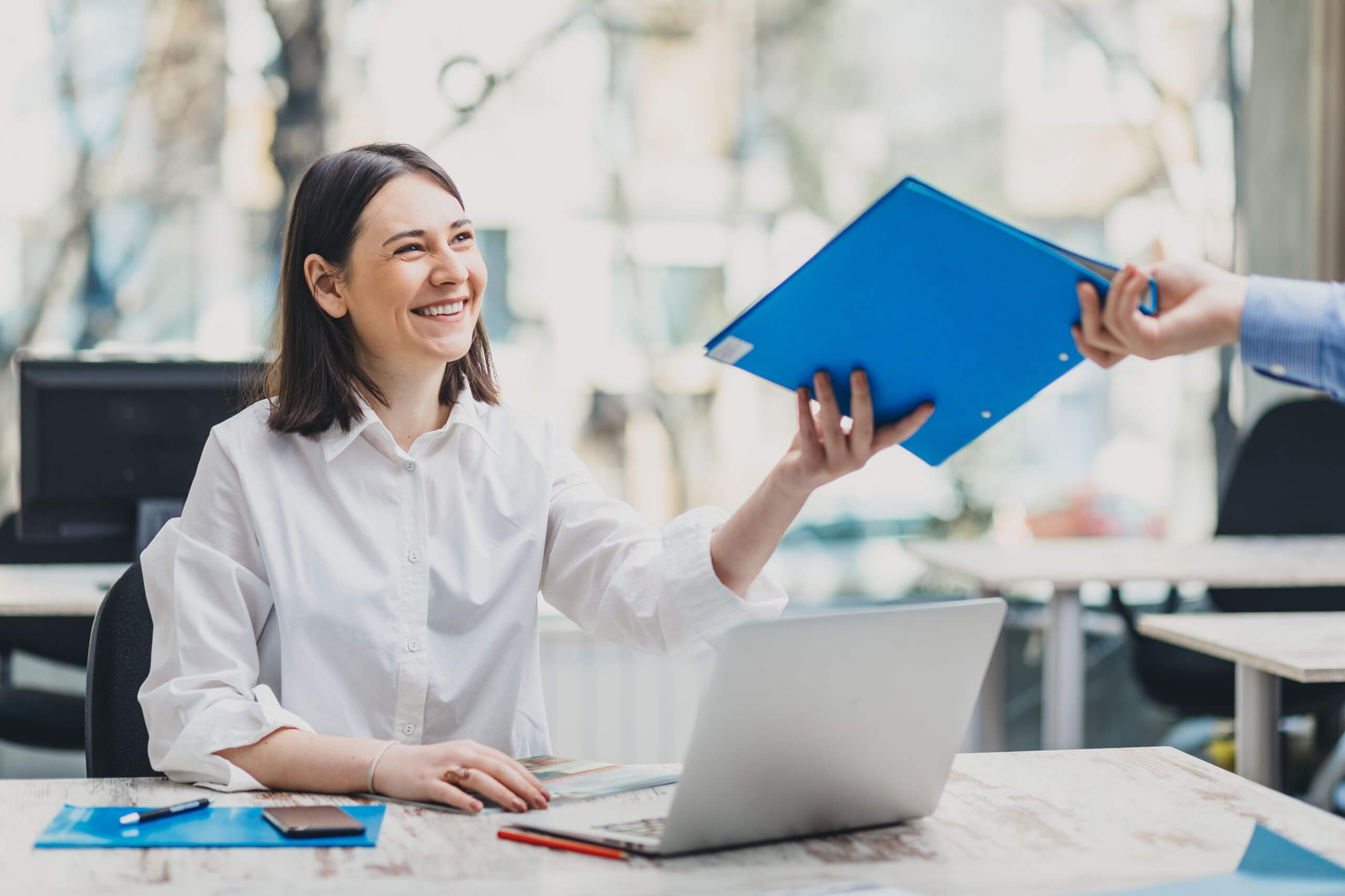 Woman at desk hands over a blue folder